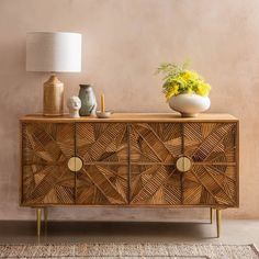 a wooden sideboard with two vases and a lamp on the table next to it