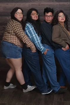 four people standing next to each other in front of a wooden wall