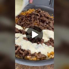 a pan filled with meat and cheese on top of a wooden table next to a knife