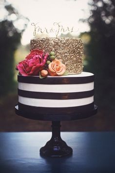 a black and white striped cake with gold glitter topper, flowers and name on it