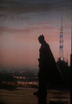 a man standing on top of a roof next to a tall building at night with the city lights in the background