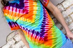 a man with long hair wearing a tie - dyed t - shirt leaning against a brick wall