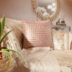 a bed with pink and gold pillows in front of a round mirror on the wall