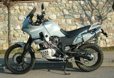 a silver motorcycle parked next to a stone wall