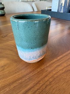 a blue cup sitting on top of a wooden table next to a book shelf with books