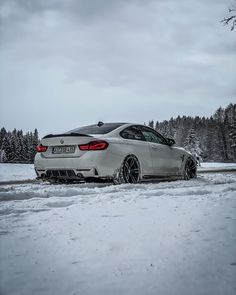 a white car is parked in the snow near some trees and bushes on a cloudy day