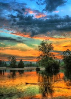 the sun is setting over a lake with trees in it and clouds reflected in the water