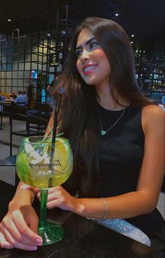 a woman sitting at a bar holding a green cocktail