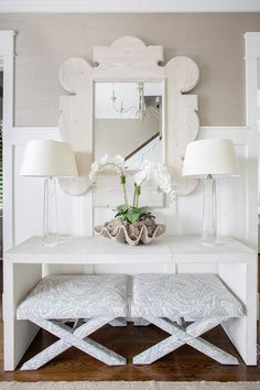 a white table with two lamps and a mirror on it's wall next to a bench