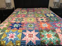 a bed with a colorful quilt on it's headboard and night stands in the background