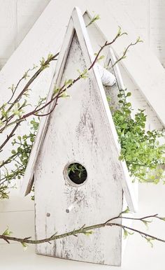 a white birdhouse sitting on top of a table next to a tree branch and potted plant