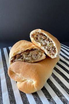 two pieces of bread with meat in it on a striped tablecloth next to a black and white wall