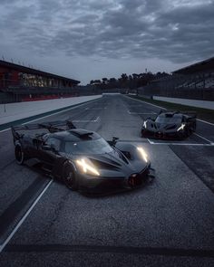 two black sports cars driving on a race track at night with lights on the front