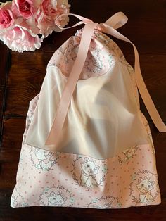 a pink flower sits next to a white bag on a wooden table with flowers in it