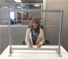 a woman sitting at a desk in an office with her hands on the table and writing