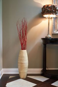 a vase with branches in it sitting on the floor next to a table and lamp