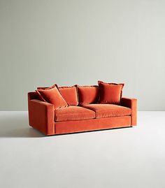 an orange couch sitting on top of a white floor next to a wall with two pillows