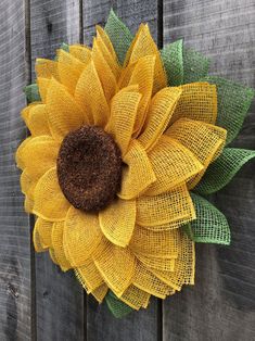 a yellow sunflower with green leaves on a wooden fence wall hanging from the side