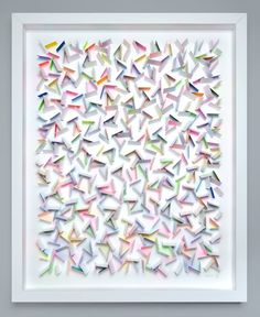 an art piece made out of folded paper with different colors and shapes on the wall