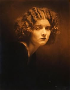 an old black and white photo of a woman with curly hair wearing a dark dress