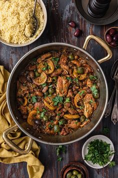 a large pan filled with meat and vegetables next to other dishes on a wooden table