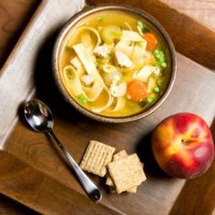 a bowl of soup, crackers and an apple on a wooden tray