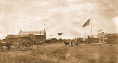 an old time photo of people and horses in the dirt with flags flying above them