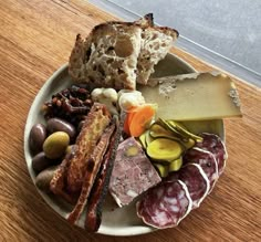 a white plate topped with meats and cheese on top of a wooden table next to a window