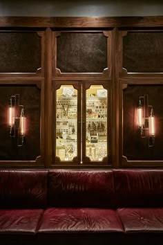 a red leather couch sitting in front of a window with wine bottles on the wall