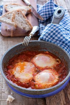 three eggs in tomato sauce with bread on the side