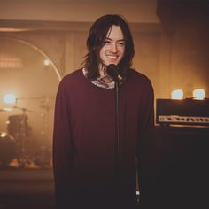 a man with long hair standing in front of a microphone and smiling at the camera