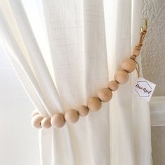 a wooden beaded necklace hanging from the side of a curtain with a name tag attached to it