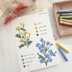 some crayons are sitting on a table next to an open book and flowers