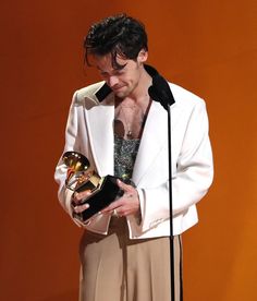 a man in a white suit holding an award and looking at his cell phone while standing next to a microphone