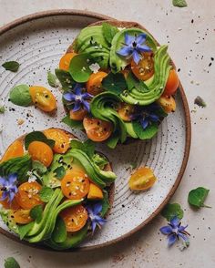 two slices of bread topped with vegetables on top of a white plate next to leaves and flowers