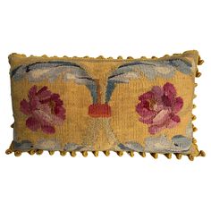 a yellow pillow with pink flowers on the front and back, sitting on a white surface