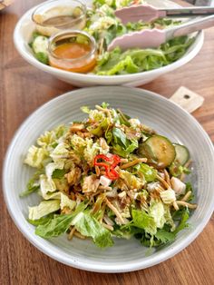 two white bowls filled with salad on top of a wooden table