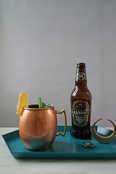 a bottle of craft beer next to a copper mug with a garnish in it