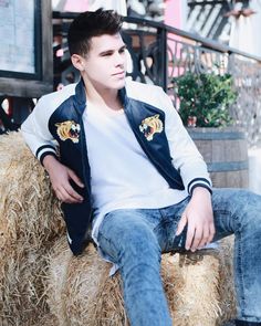 a young man sitting on top of hay bales wearing jeans and a leather jacket