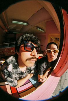 a man and woman taking a selfie in front of a colorful wall with round mirrors