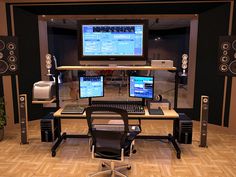 a computer desk with two monitors and speakers on top of it in front of a wall mounted speaker system