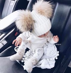 a baby sitting in the back seat of a car wearing a white hat and coat