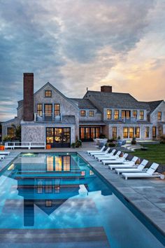 a large house with a swimming pool and lounge chairs around the perimeter, at dusk