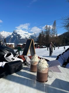 two cups of coffee sitting on top of a table next to snow covered mountains in the background