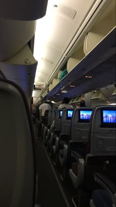 the inside of an airplane with many seats and televisions on it's walls