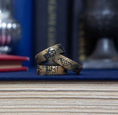 two gold wedding bands sitting on top of a wooden table next to a stack of books