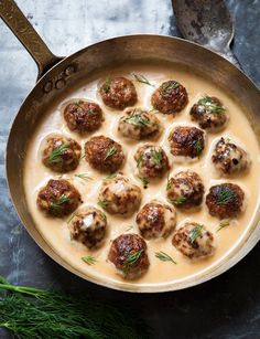 a pan filled with meatballs covered in gravy and garnished with fresh herbs