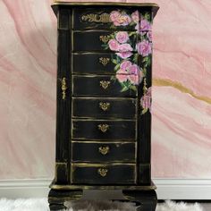 a black dresser with pink flowers painted on the front and bottom drawers, sitting against a pink wall