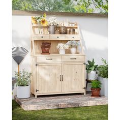 a wooden cabinet sitting on top of a grass covered ground next to potted plants