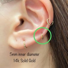 an image of a woman's ear with three small gold hoops on it